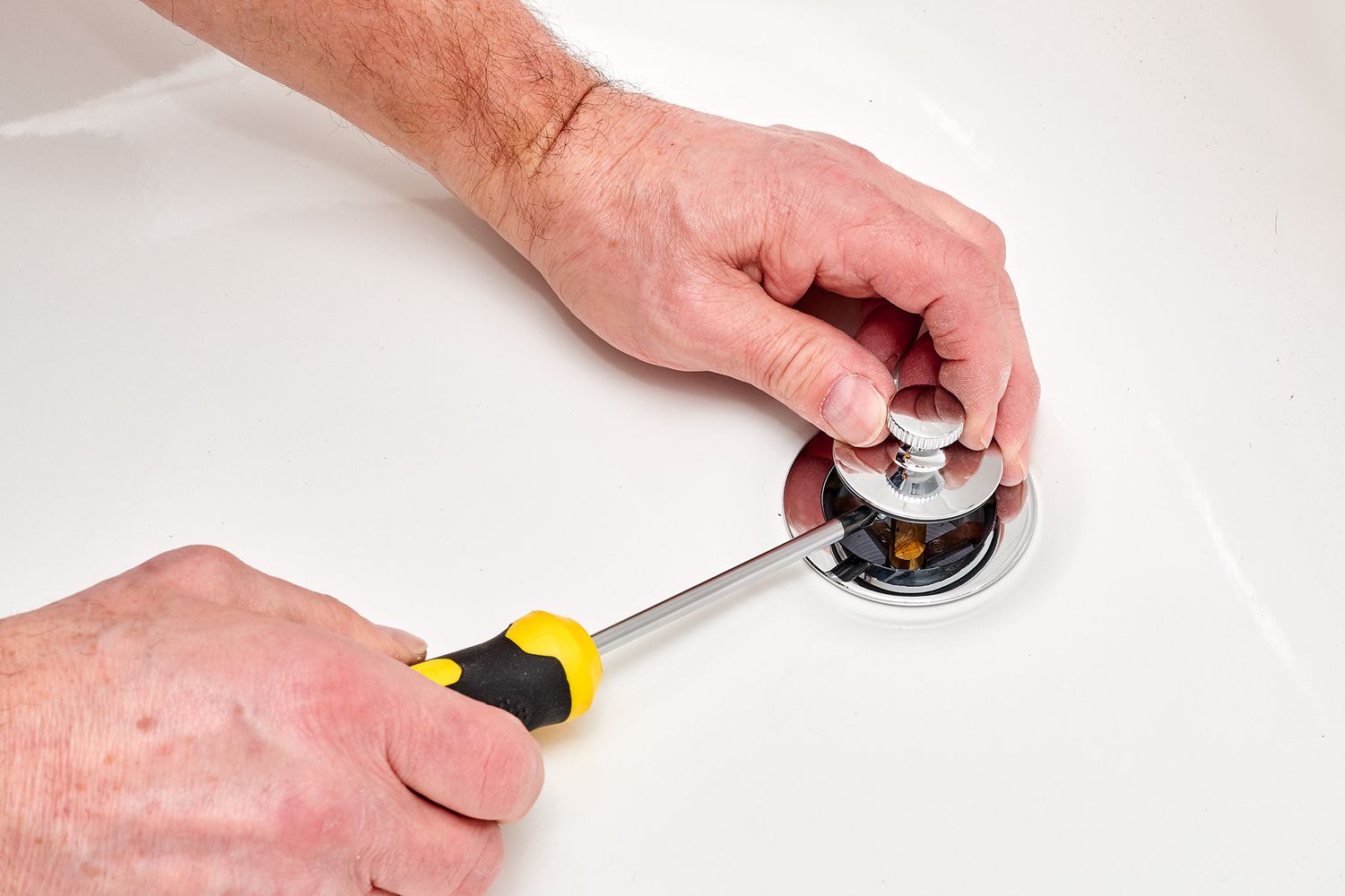 Push-and-pull drain stopper lifted from drain hole with screwdriver