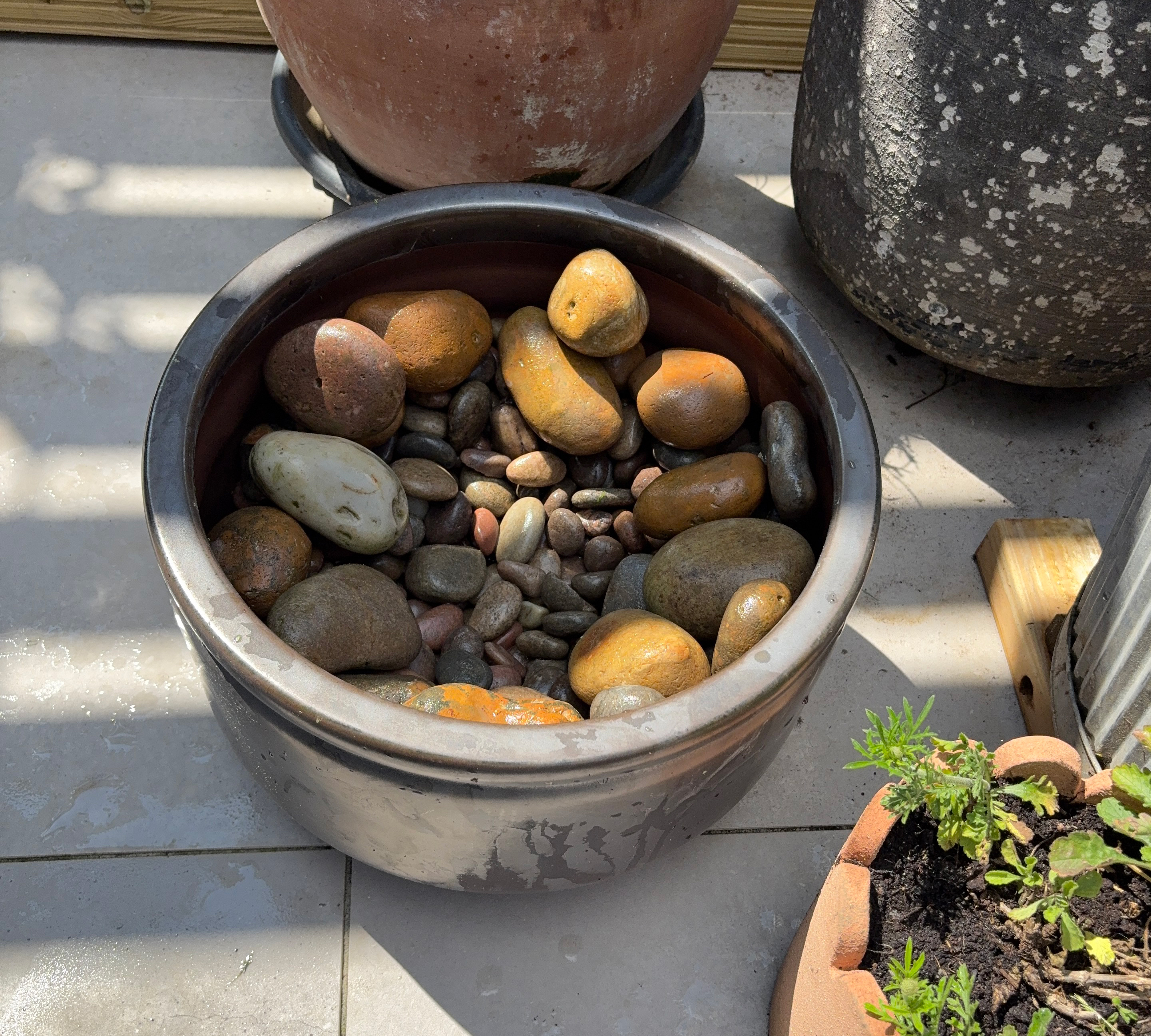 Grey ceramic planter on a grey paved patio filled with pebbles and cobbles