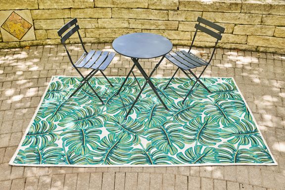 Two chairs and a table placed on Rifle Paper Co. Veranda Monstera Cream Outdoor Rug