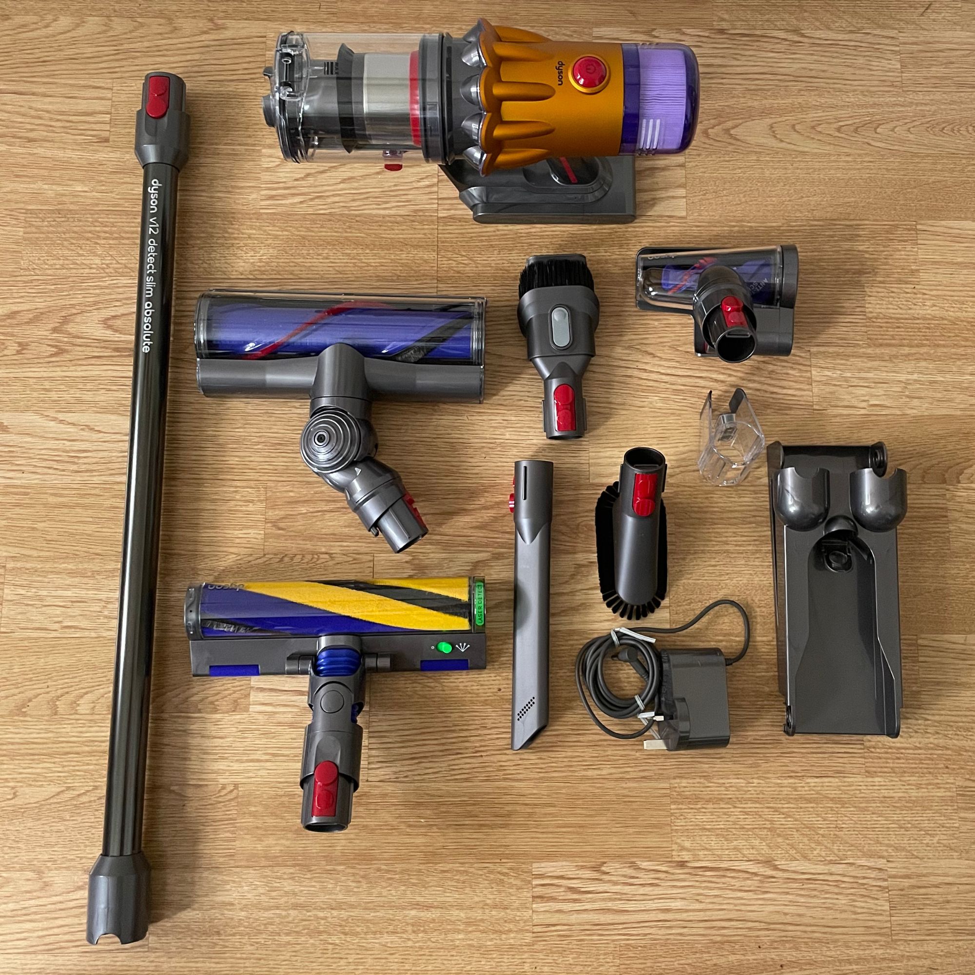 Components of the Dyson V12 Detect Slim Absolute laid out on a wooden floor