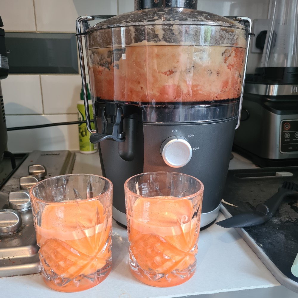 Nutribullet juicer on a kitchen counter filled with pink juice with 2 glasses of juice