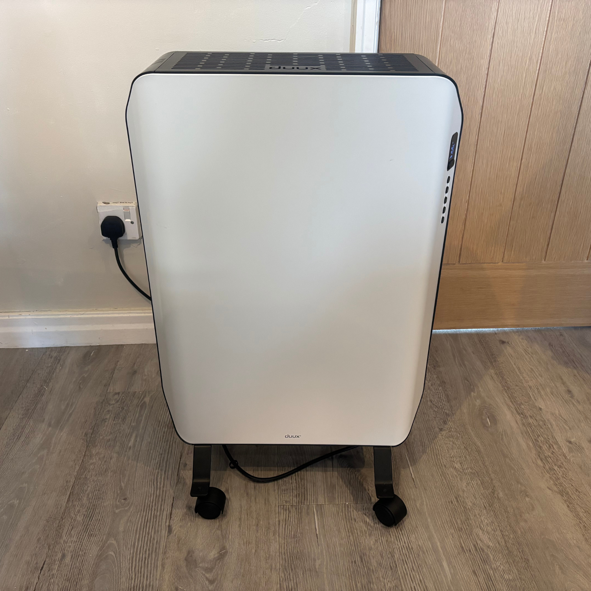 white Duux Edge Oil 2000W Oil-Filled Radiator side view in front of a wooden door and cream wall