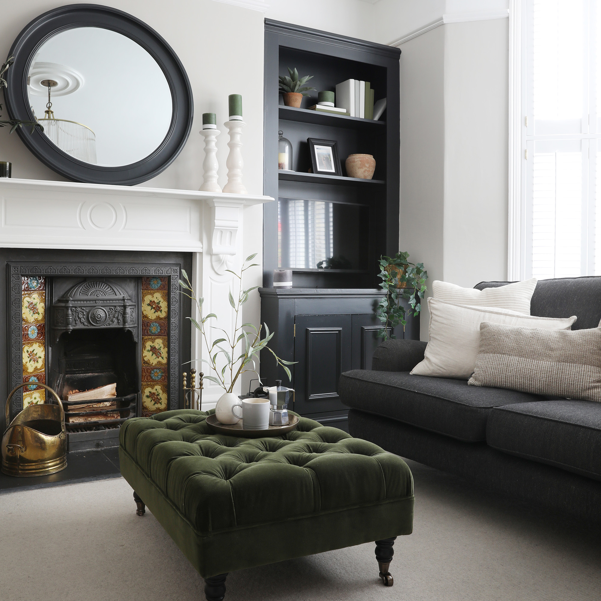 neutral living room with pale walls, carpet and grey sofa with a victorian fireplace, green ottoman-style footstool and dark grey alcove cupboards