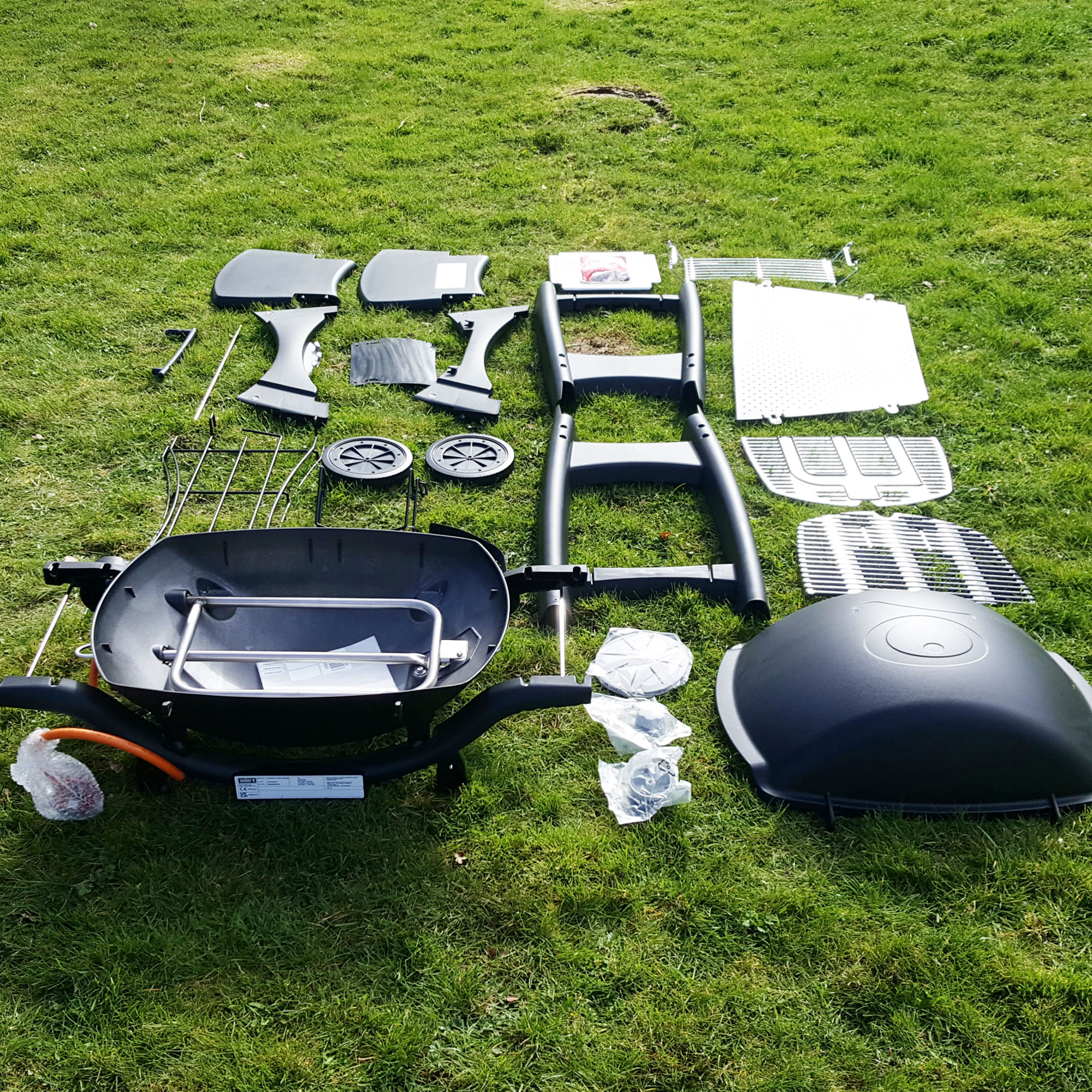 The Weber Q3200 BBQ in pieces on a grass lawn ready for assembly 