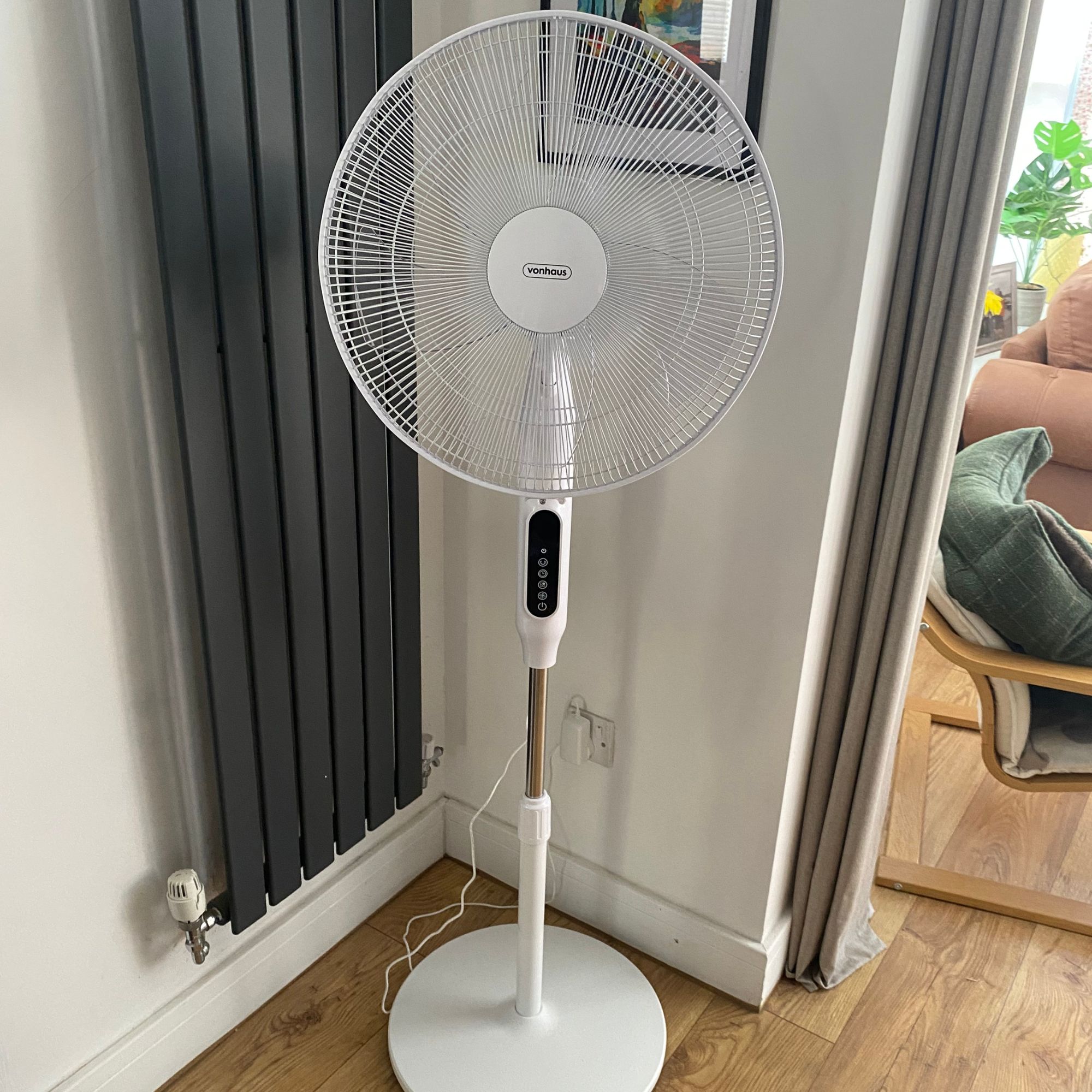 Vonhaus 16'' pedestal fan at full height in the corner of a room next to a vertical radiator