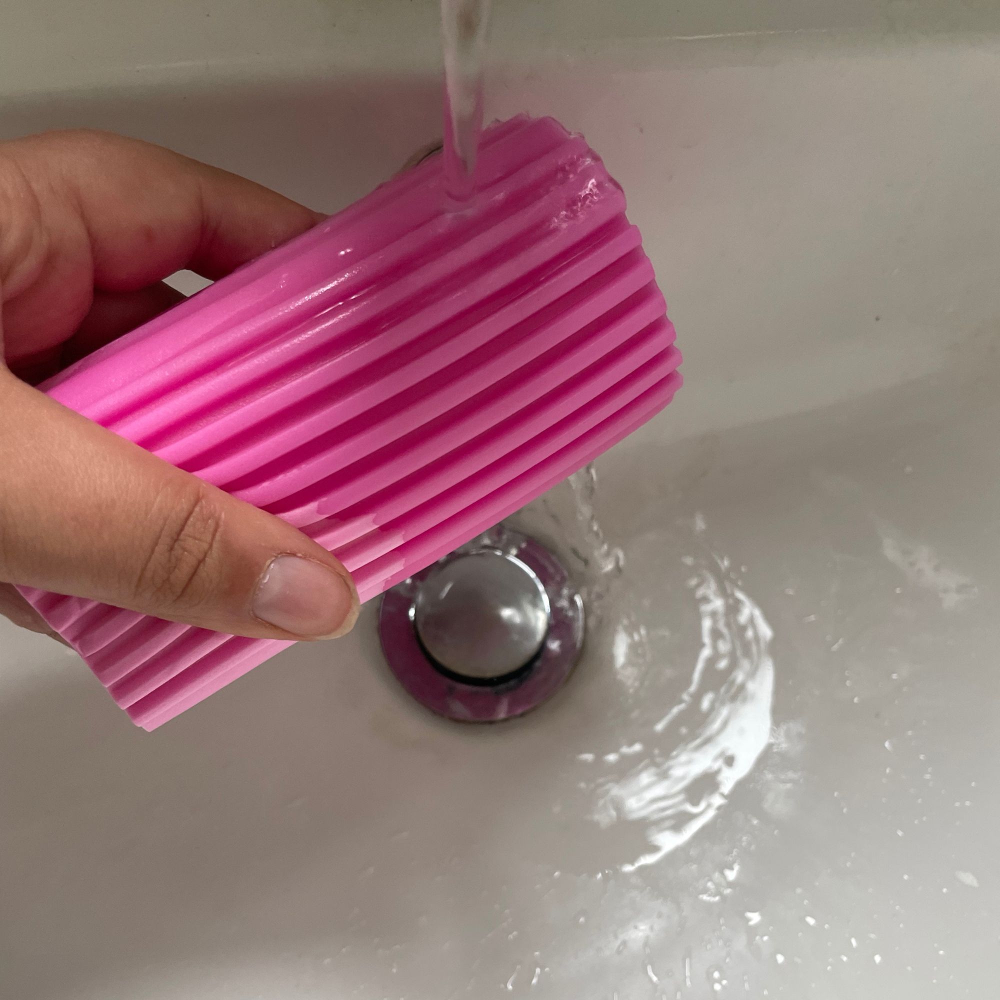 Holding pink Damp Duster under running water in a white sink with silver plug hole
