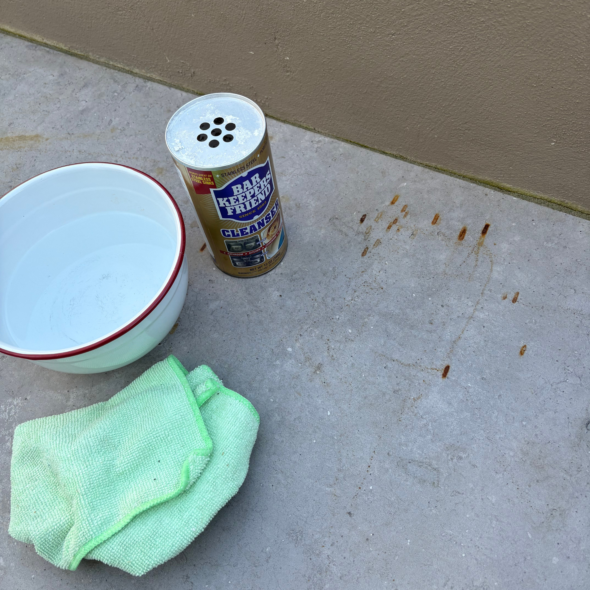 Bar Keeper's Friend, bowl of water and green micro-firbre cloth next to the patio rust stain.