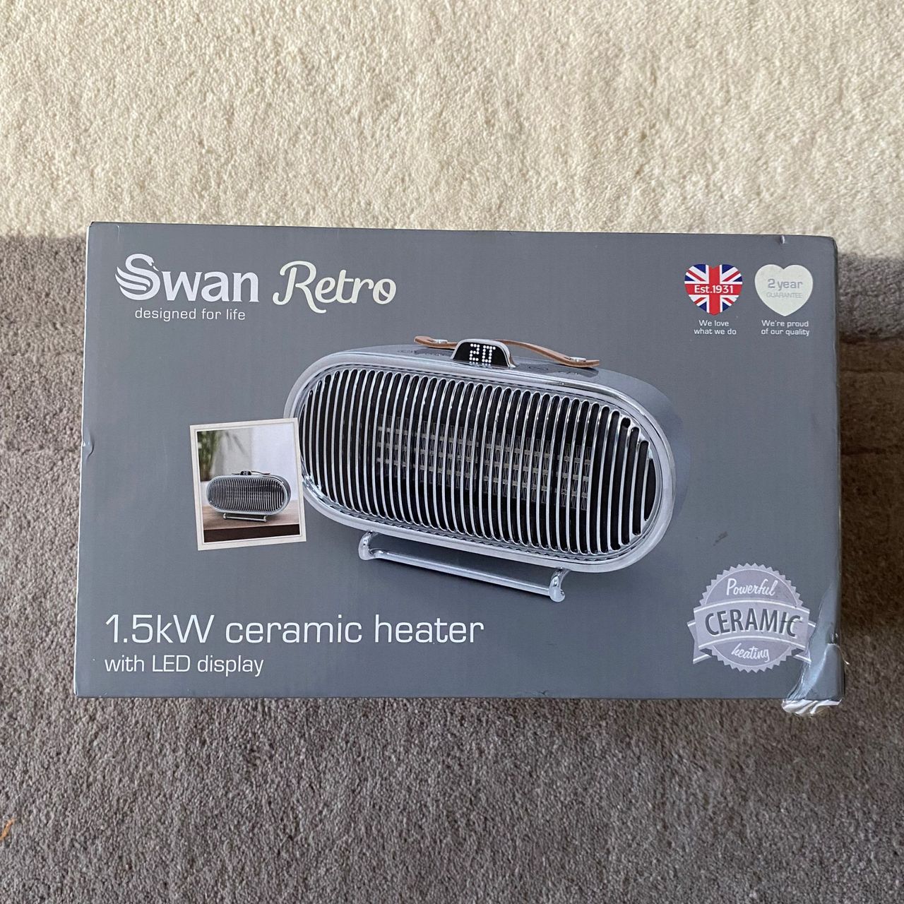Outer packaging of the Swan 1.5kW Retro Ceramic Heater, sitting on a grey and cream rug